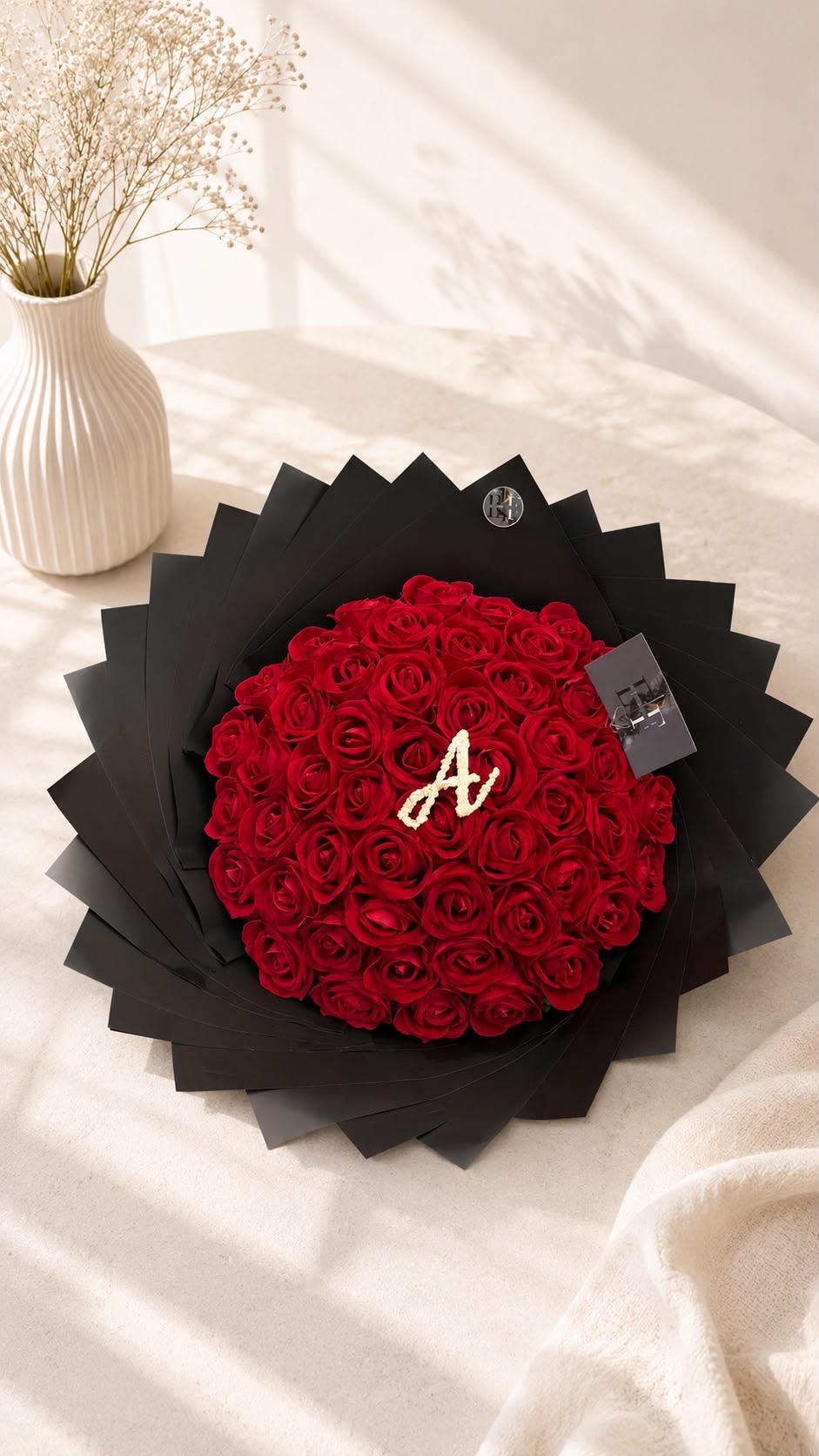Grand red rose bouquet with pearl initial 'A' in dramatic black fan wrap on marble