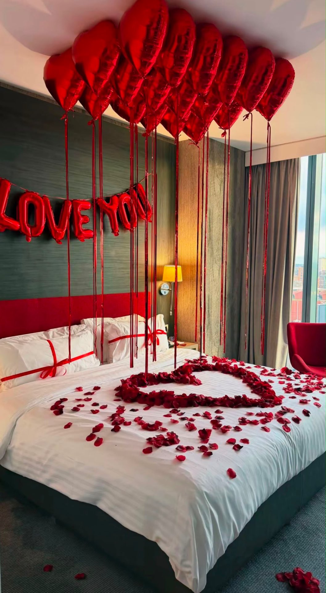 Love You suite with red heart balloons and a heart of rose petals on the bed